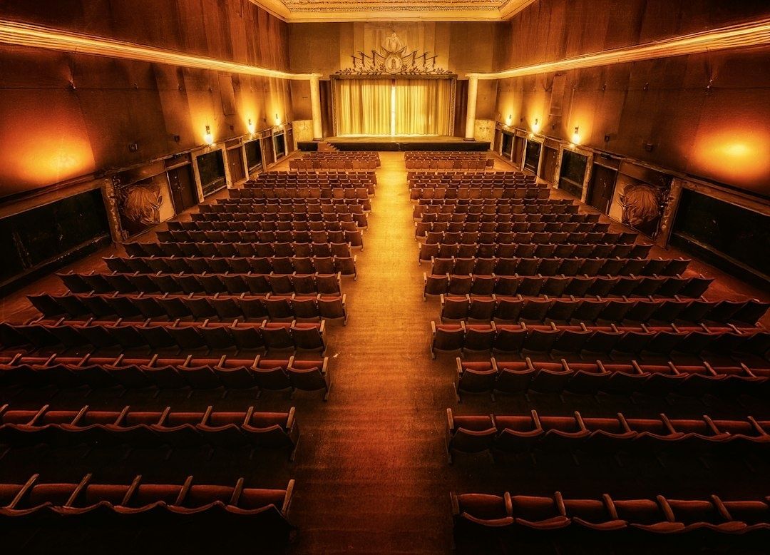 Leerer, warm beleuchteter Theatersaal mit Reihen roter Sitze und Bühne