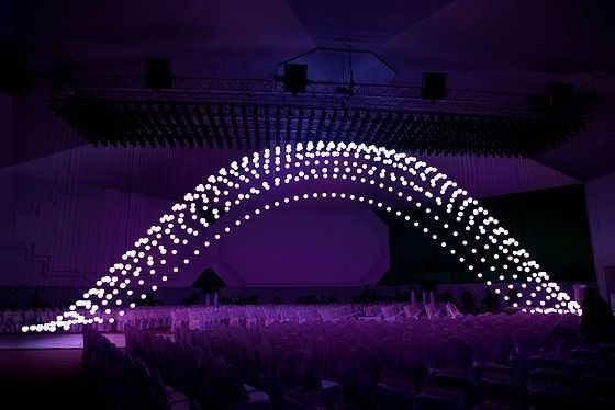 Leuchtende, bogenförmige Bühneninstallation über einem bestuhlten Saal