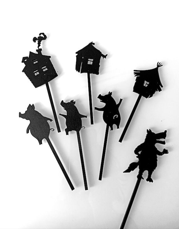 Schwarze Schattenspielfiguren mit Häusern, Tieren und Hexengestalten